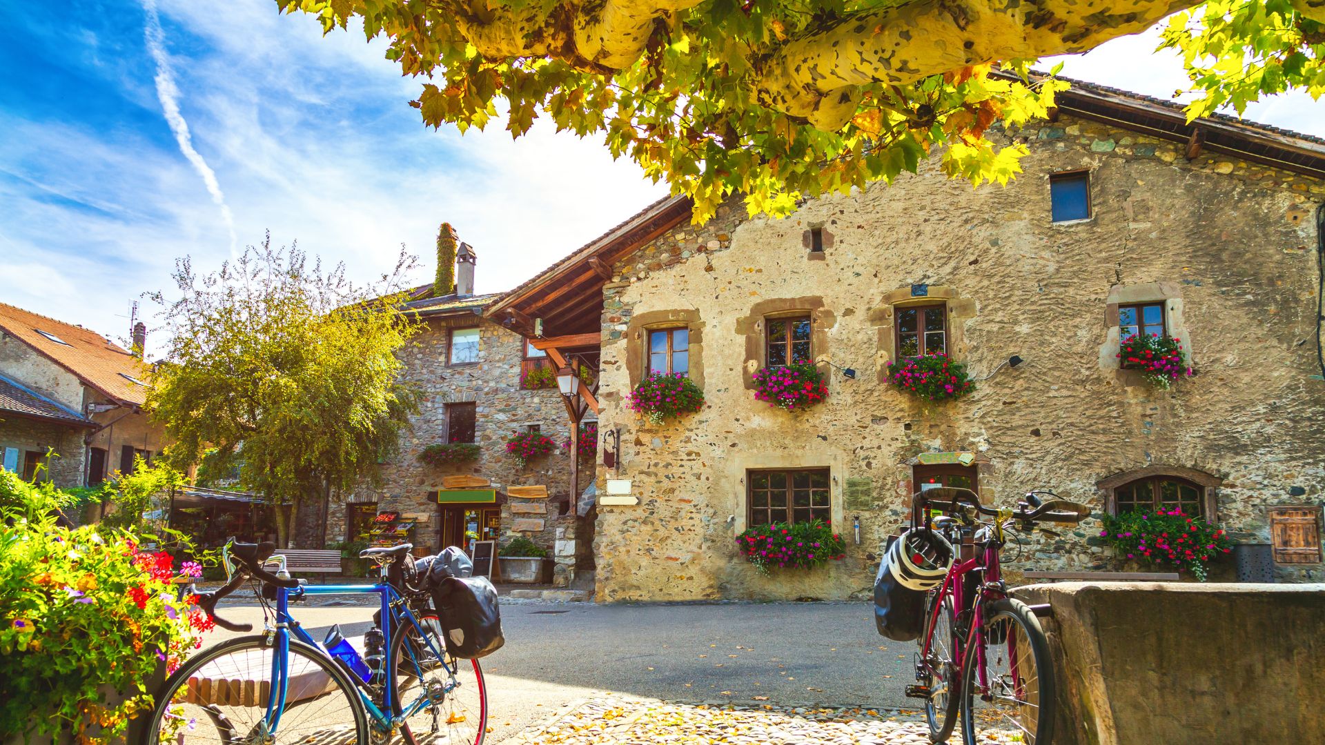 "Scène pittoresque d'une vieille ville dans le Genevois, avec un bâtiment en pierres apparentes orné de fenêtres fleuries de géraniums rouges.