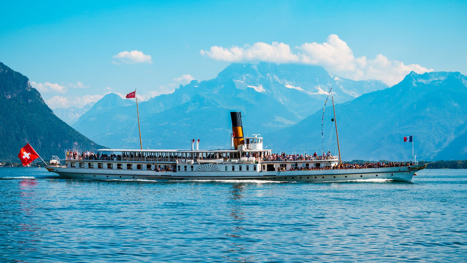 Bateau à vapeur sur le Lac Léman avec des montagnes en arrière-plan par une journée ensoleillée.