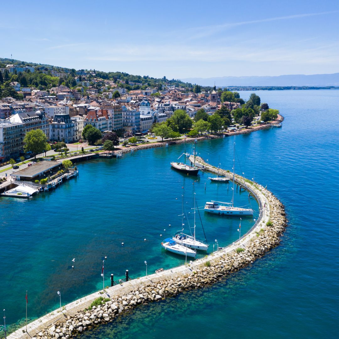 Vue aérienne au bord du Lac Léman avec une marina courbée et plusieurs voiliers amarrés.